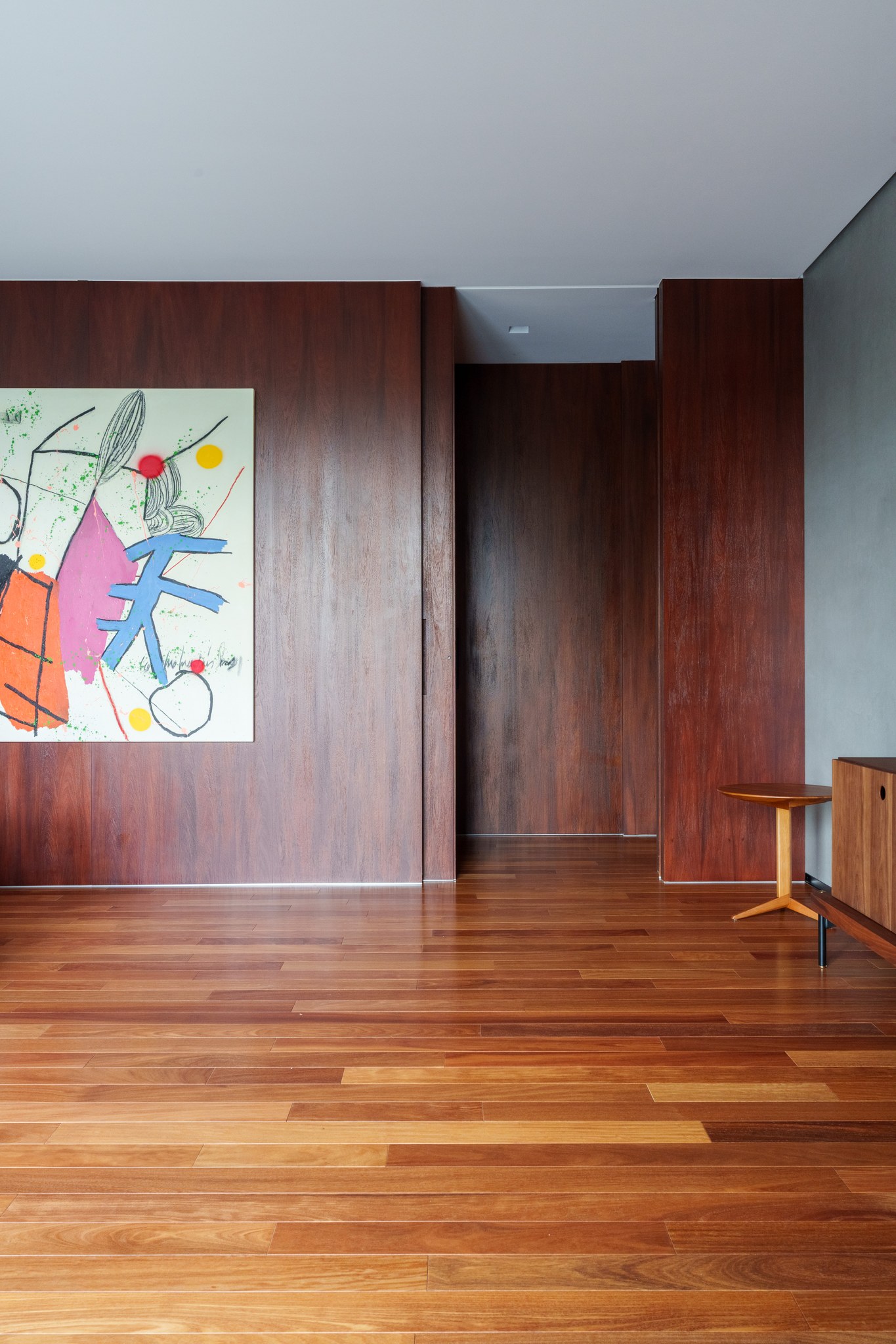 Corredor em madeira escura com obra de arte colorida e mesa de apoio