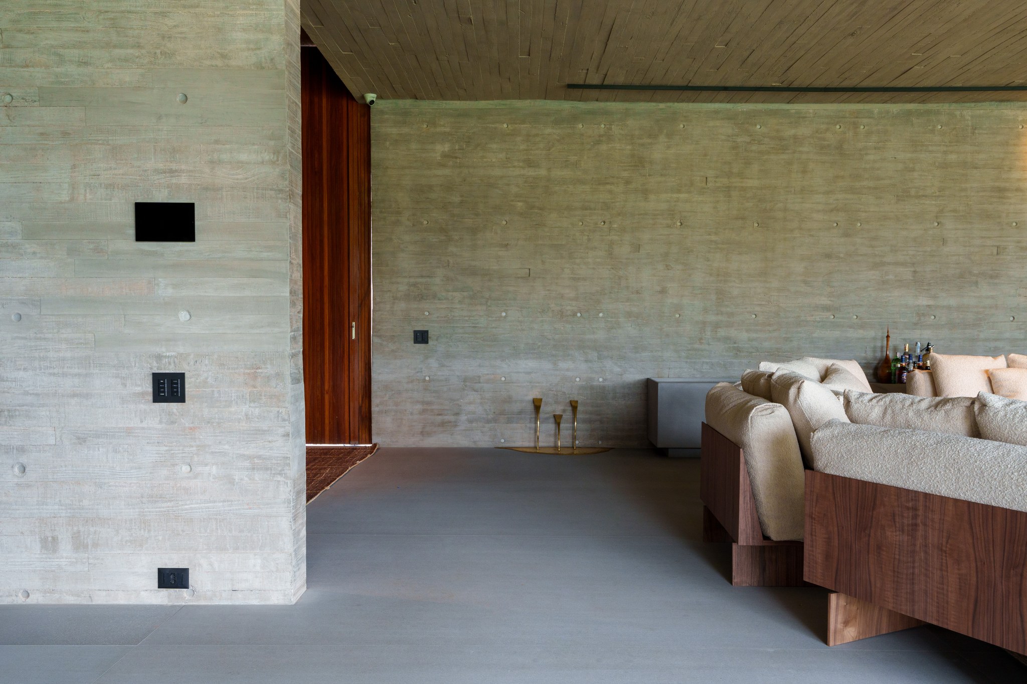 Sala de estar em concreto aparente, com sofá de madeira maciça e porta pivotante para o pátio interno