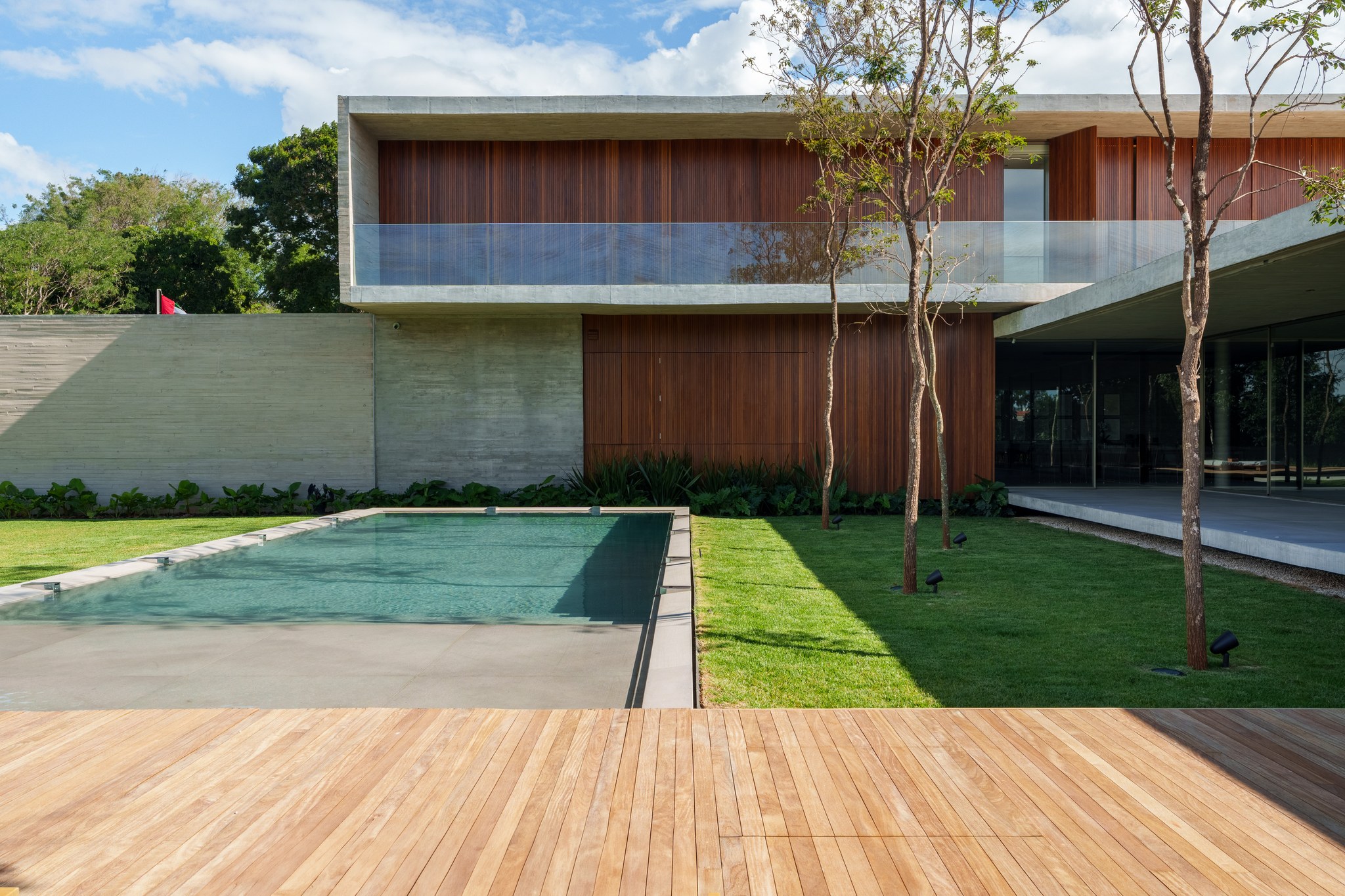 Fachada dos fundos em dois pavimentos, com balanço de concreto, revestimento em madeira ripada e piscina espelhada
