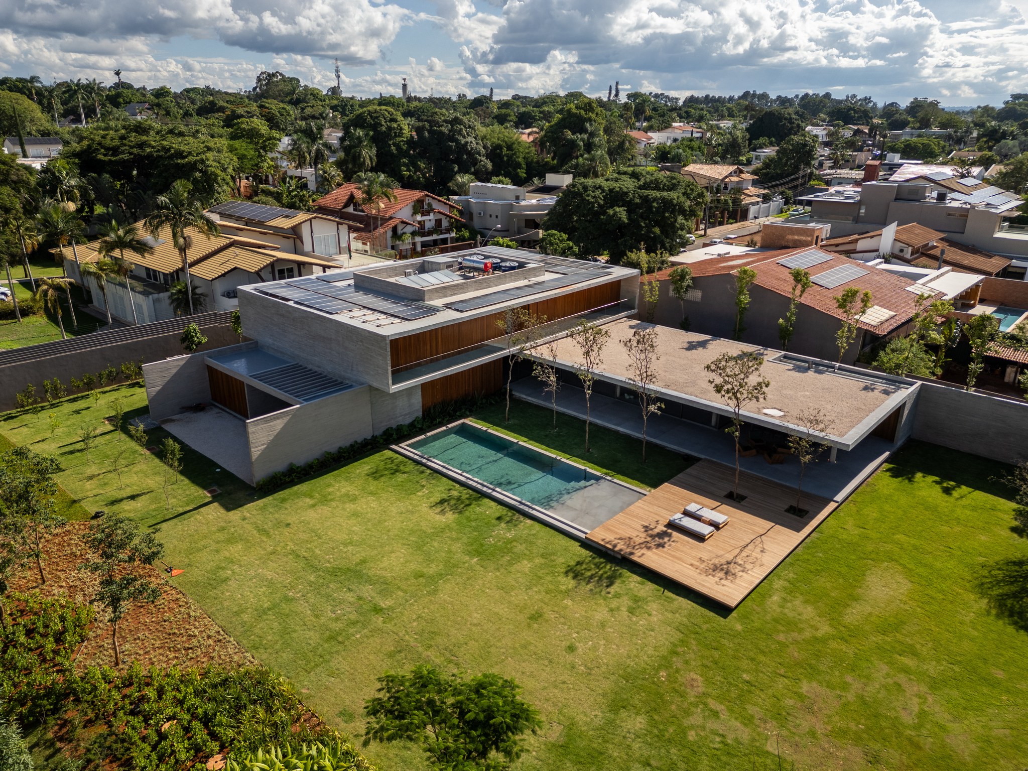 Vista aérea da casa com piscina, deque de madeira e telhado ajardinado entre casas vizinhas