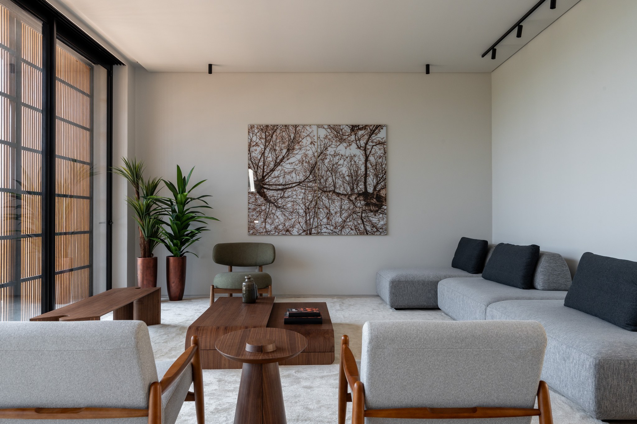 Sala de estar com sofás modulares cinza, poltrona verde-musgo e fotografia de árvore emoldurada