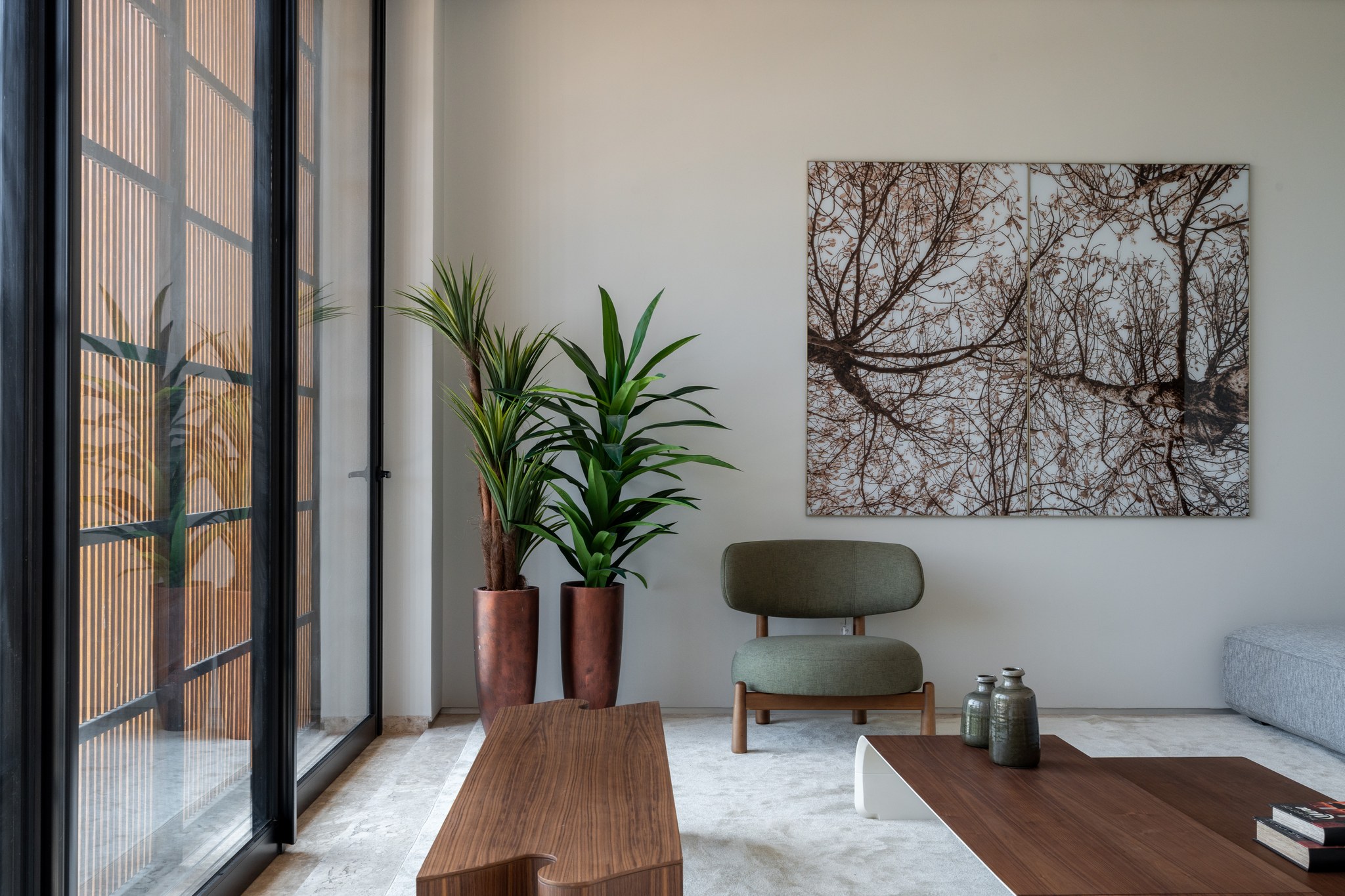 Detalhe da sala de estar com esquadria em brise metálico, plantas em vasos de cobre e fotografia de galhos