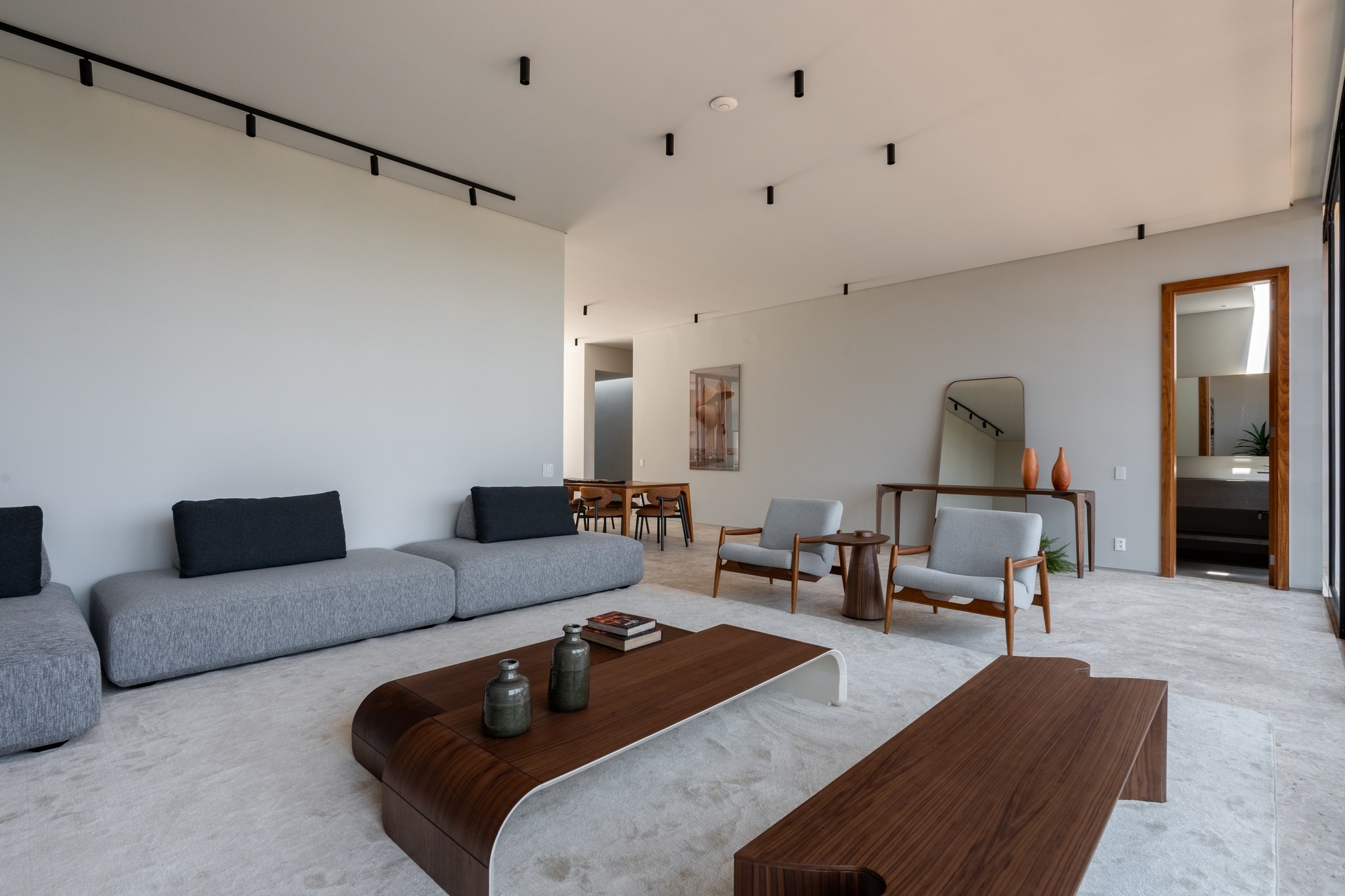 Sala de estar ampla com sofás modulares, poltronas de madeira e vista para a sala de jantar ao fundo