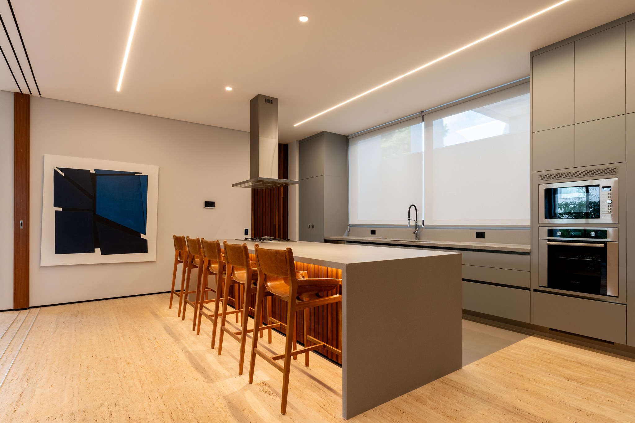Cozinha gourmet com ilha em pedra escura, banquetas de couro caramelo e quadro abstrato azul
