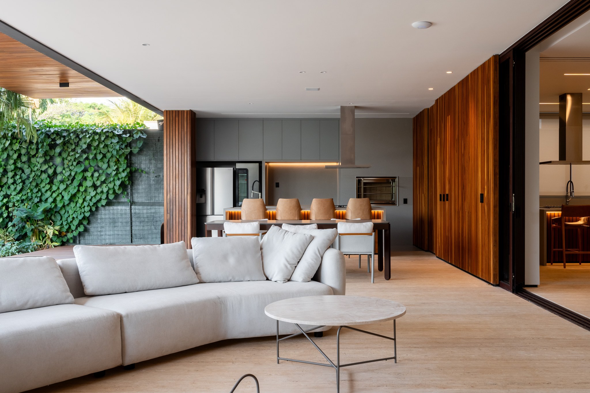 Sala de estar aberta para o jardim, com sofá bege modular e parede em ripas de madeira ao fundo