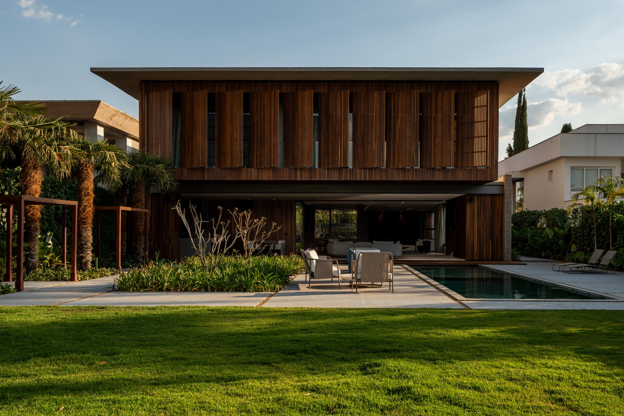 Fachada dos fundos ao entardecer, com piscina, jardim e sala de estar integrada iluminada