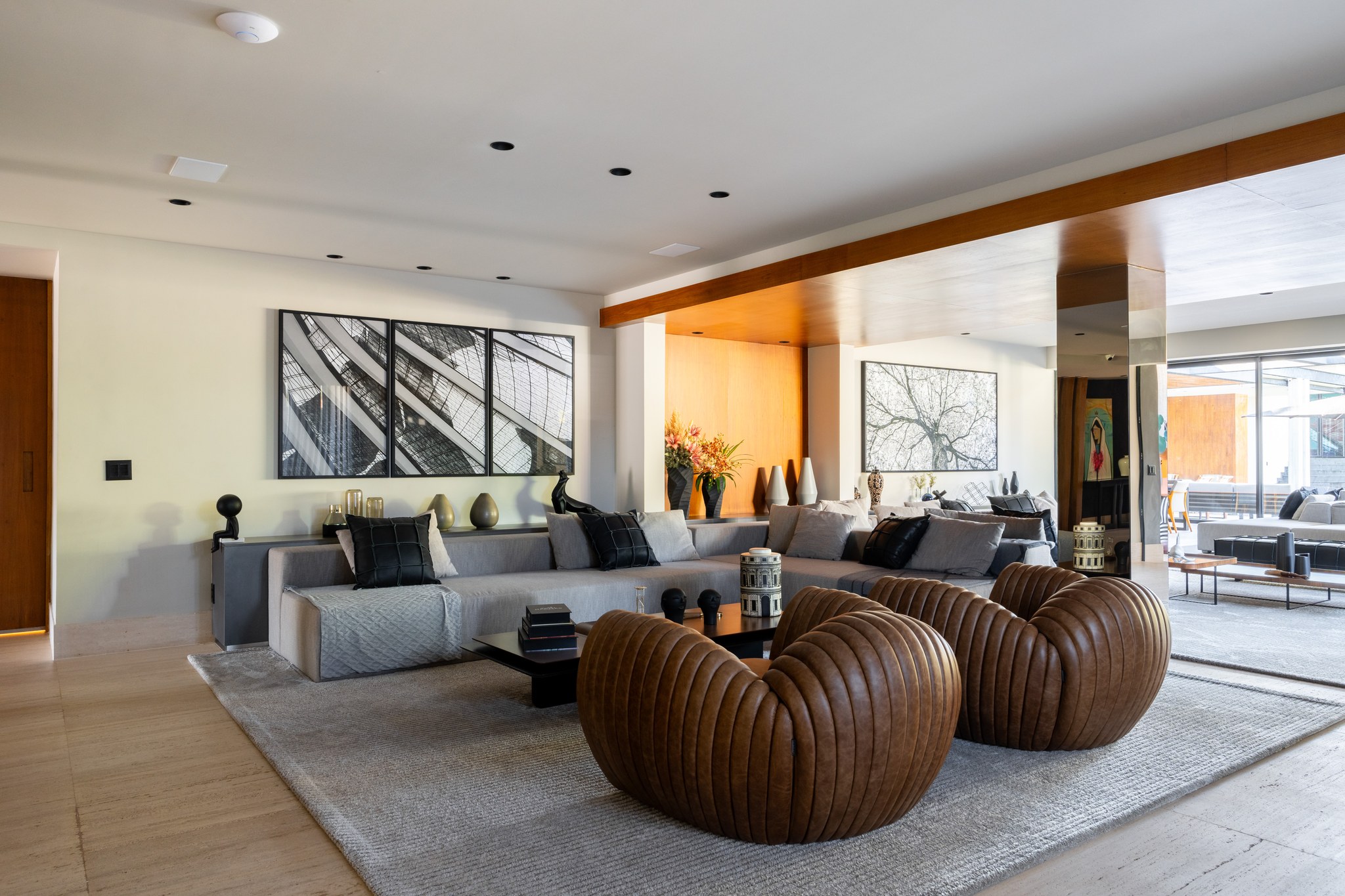 Sala de estar com sofá modular cinza, poltronas de couro caramelo e retrato fotográfico de árvore
