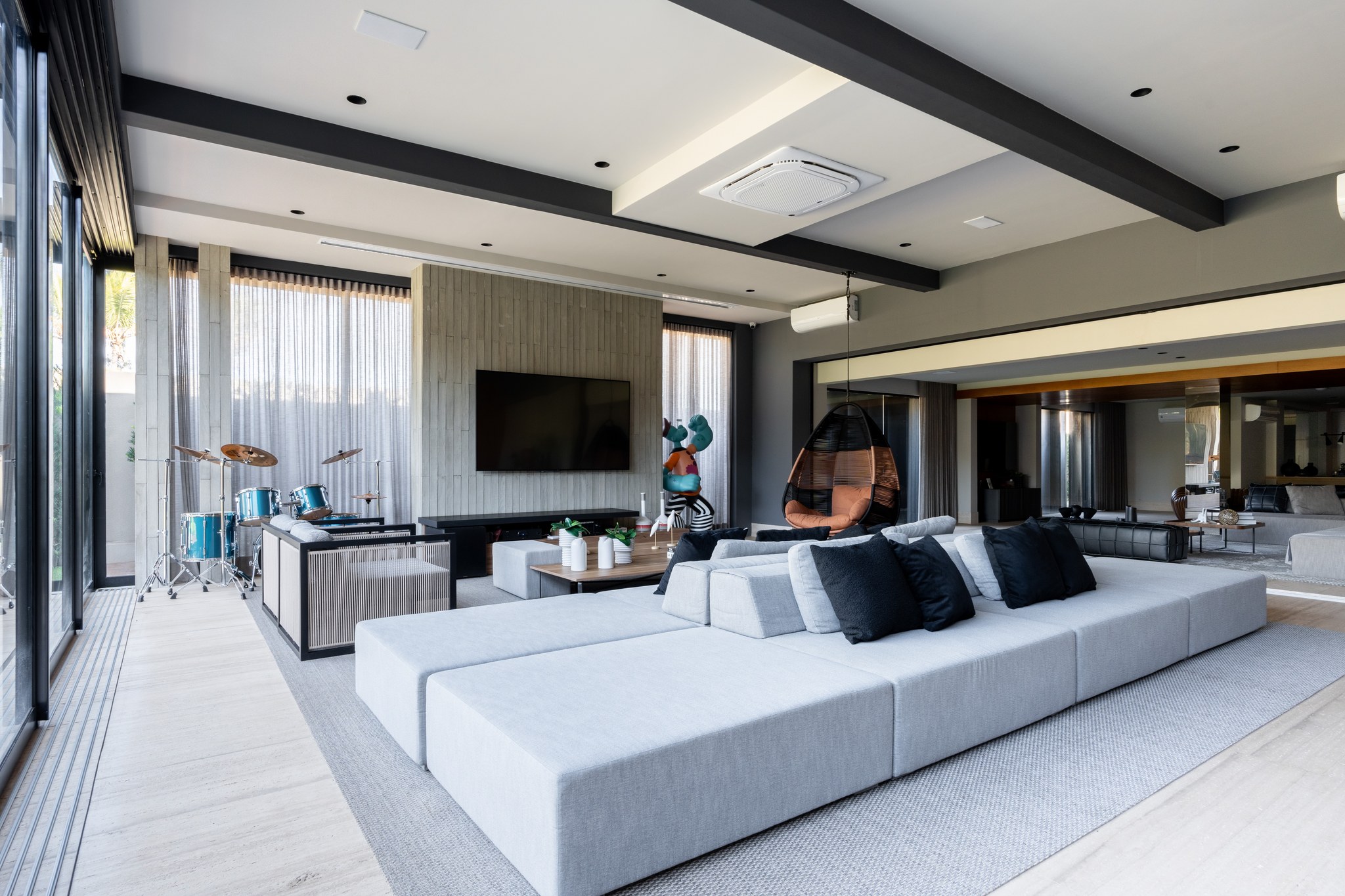 Área de estar com bateria musical, TV de parede e cadeira suspensa junto ao sofá modular