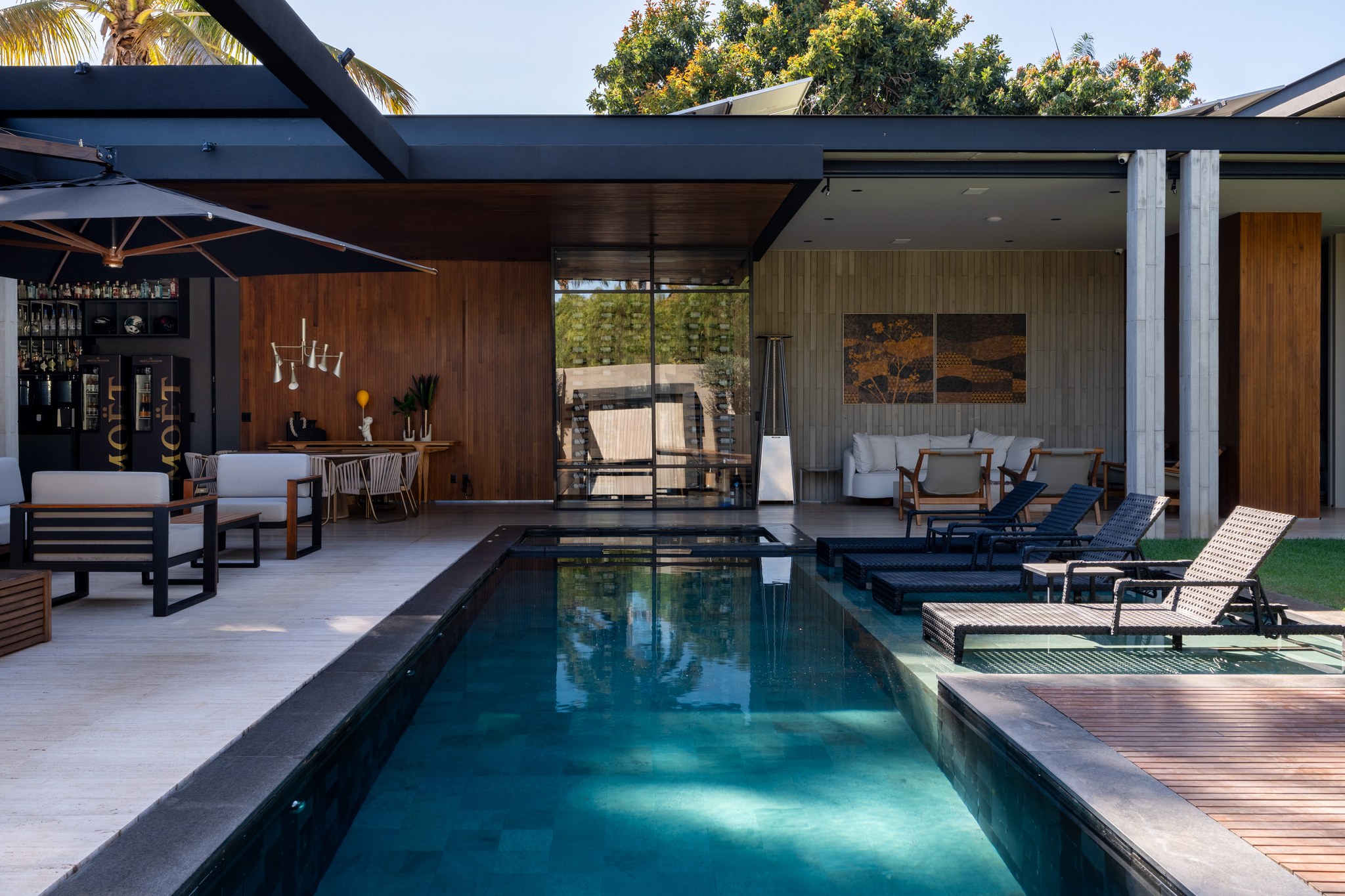 Fachada dos fundos com piscina, terraço coberto e bar externo iluminado ao entardecer