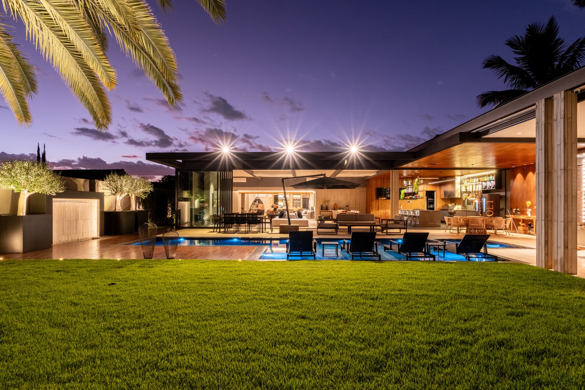 Fachada dos fundos ao entardecer, com piscina iluminada, terraço coberto e bar externo