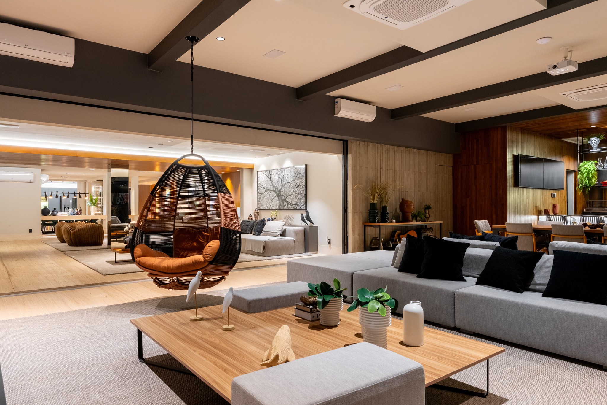 Sala de estar à noite, com cadeira suspensa iluminada e sofá modular cinza ao fundo