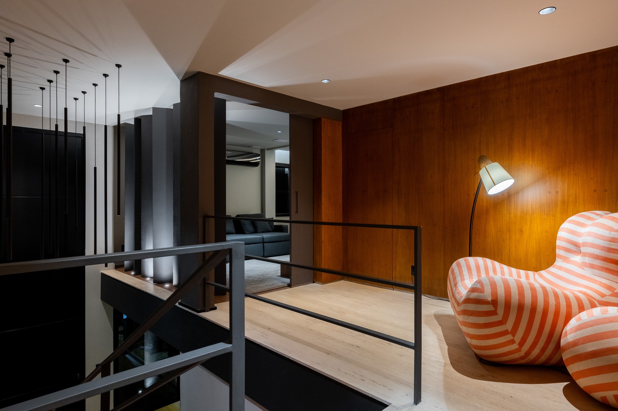 Mezanino com poltrona listrada, luminária de piso e parede em madeira, sobre a sala de estar