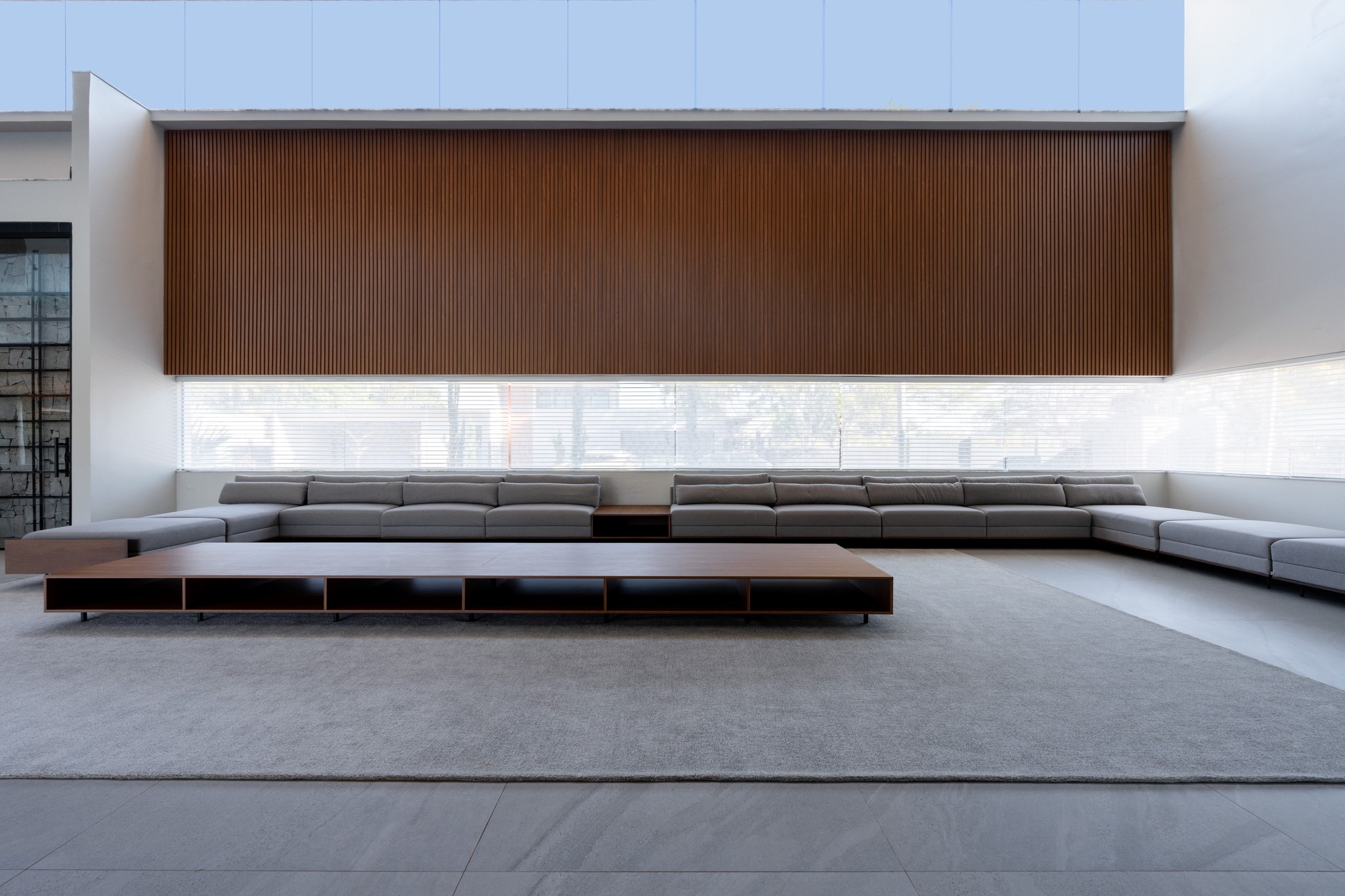 Sala de estar minimalista com sofás cinza em L, marcenaria em madeira ripada e móvel baixo com nichos
