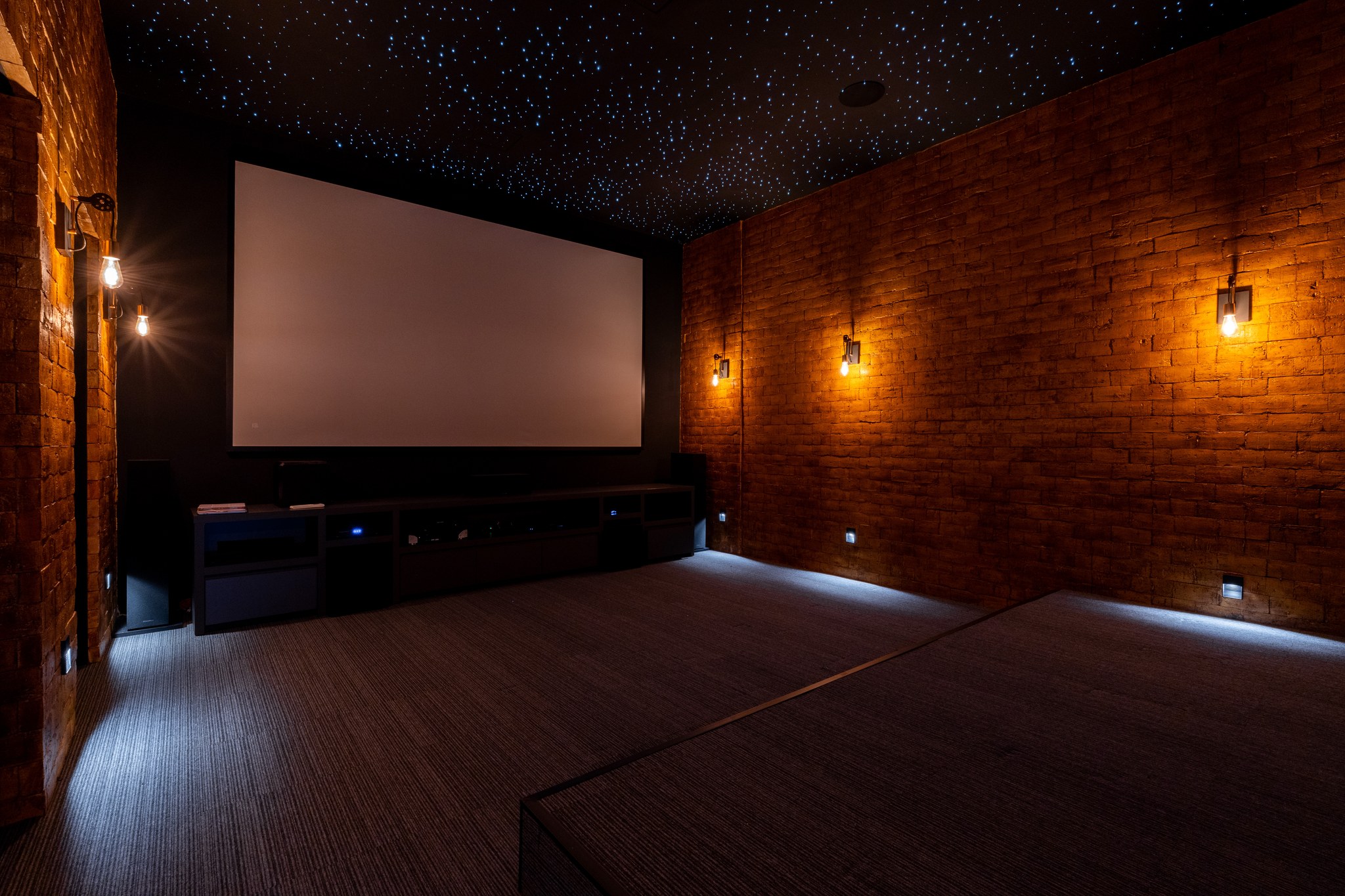 Home theater com parede em tijolo aparente, telão de projeção e teto estrelado