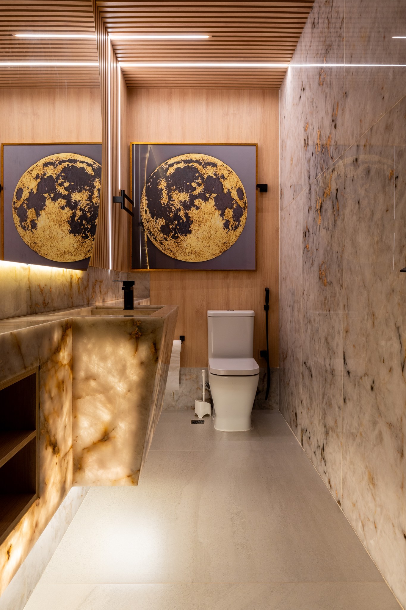 Lavabo com bancada em ônix iluminado, torneira preta e quadros da lua emoldurados em dourado