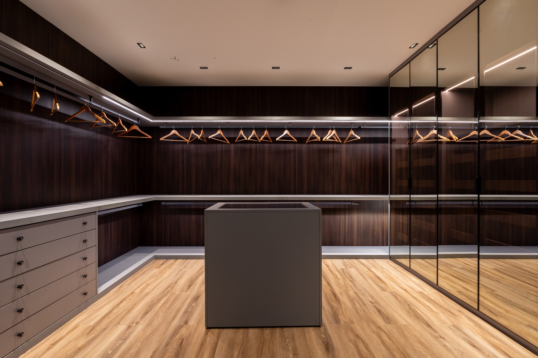 Closet com araras de metal, cabideiros de madeira e espelhos até o teto