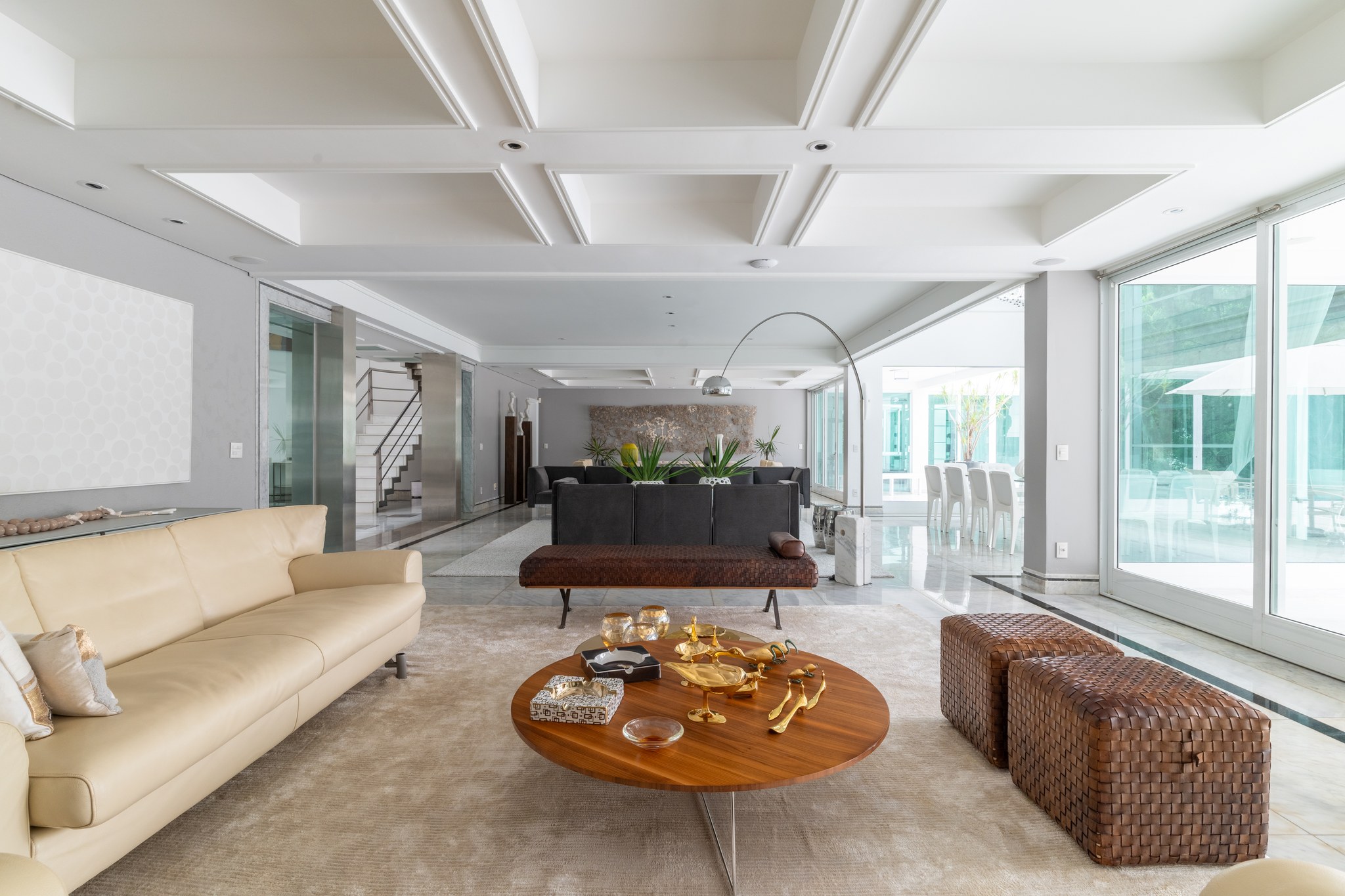 Sala de estar ampla com sofá bege, pufes trançados em couro e mesa lateral com peças em metal dourado